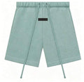A pair of sage green sweat shorts with a drawstring waist, side pockets, and 'ESSENTIALS FEAR OF GOD'  