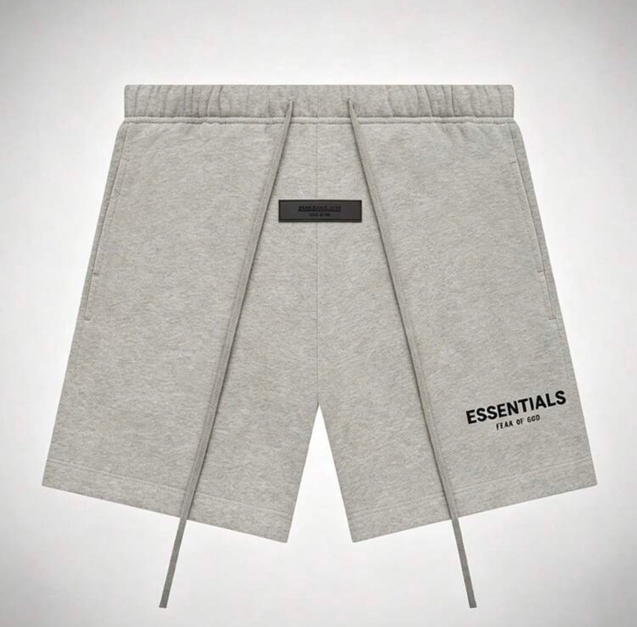 Light gray heather sweat shorts with an elastic drawstring waist, a black central label, and 'ESSENTIALS FEAR OF GOD' 